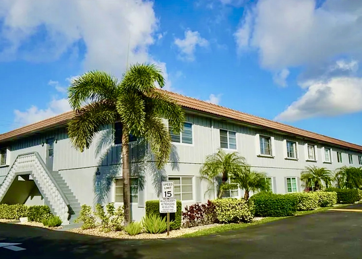 Front view of a two-story condominium complex with palm trees and a 15 MPH sign in Oakland Park, Florida.